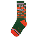 A pair of orange, green, and white ribbed gym socks with text 'HOME IS WHERE THE WEED IS' printed on the side.