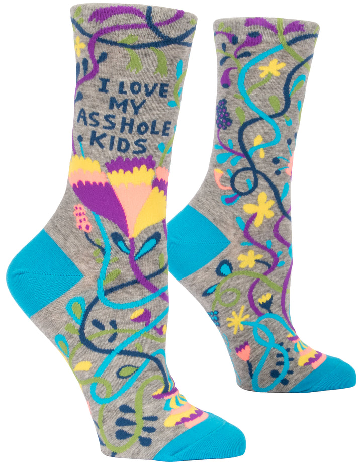 Blue Q crew socks. Greay with bright blue accents on the toe and heel. The sock is covered in a purple, teal, yellow and navy pattern. In navy on the top portion of the sock it reads "I love my asshole kids"