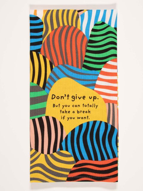 A Blue Q dish towel with a abstract wavy striped pattern in color blocks of red, yellow, orange, blue and green. A solid yellow blob in the center contains text that reads "Don't give up. But you can totally take a break if you want."