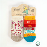 Two pairs of baby socks with humorous text on a Blue Q packaging.