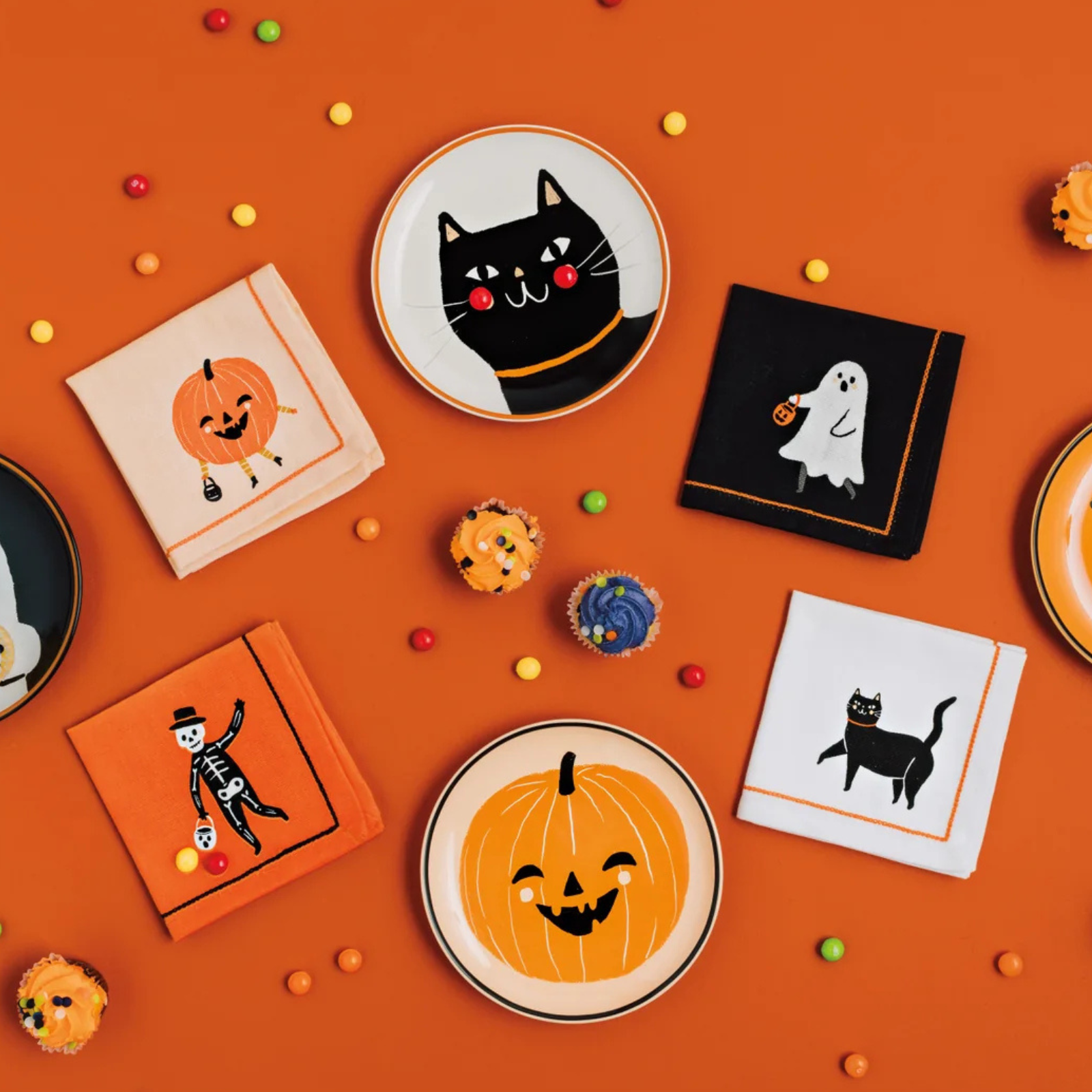 Halloween-themed plates and napkins on an orange background with small decorative items.