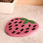 Pink strawberry-shaped wool trivet on a light-colored counter