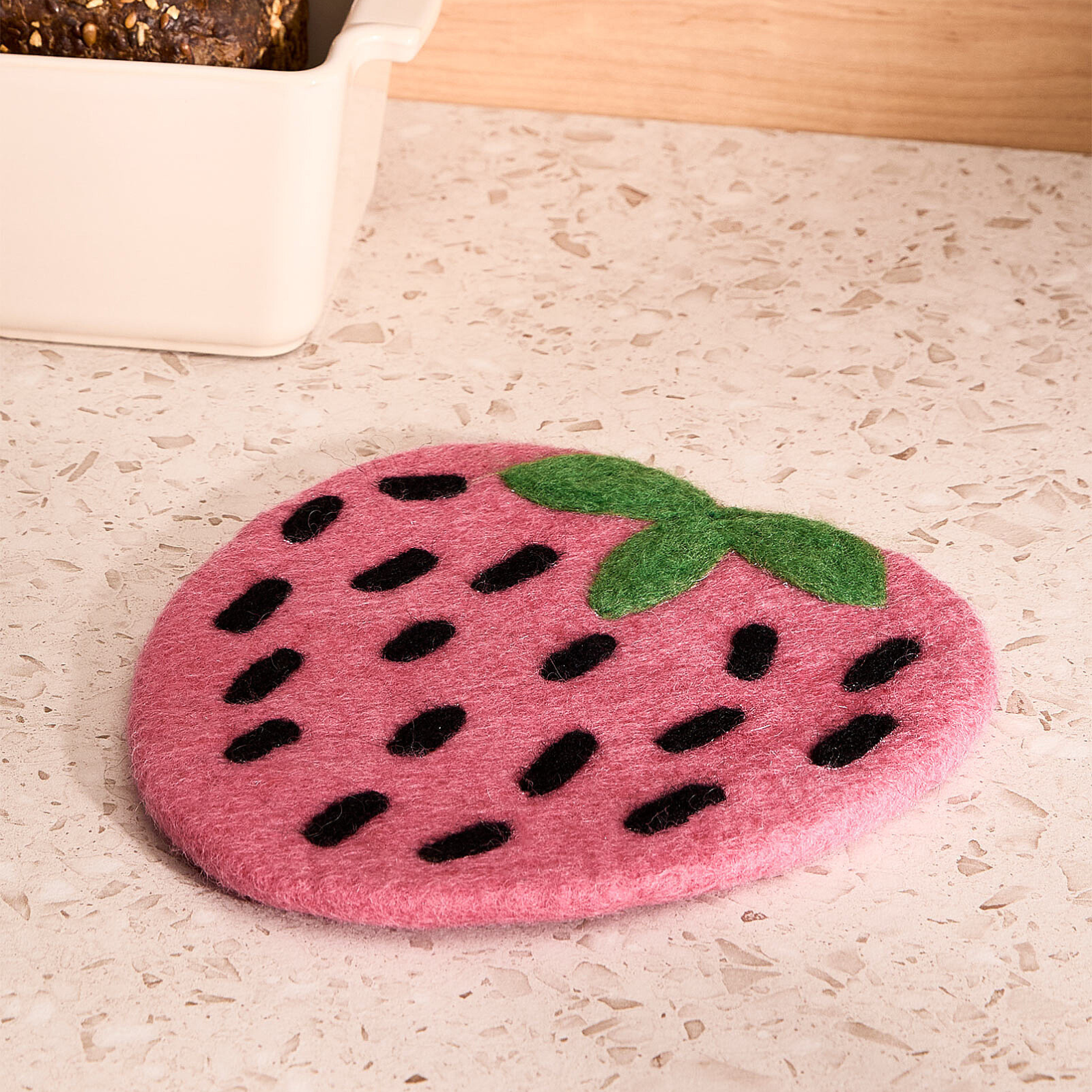 Pink strawberry-shaped wool trivet on a light-colored counter