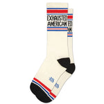 A pair of white gym crew socks with blue and red stripes and the text 'EXHAUSTED AMERICAN ED' on the ankle area.