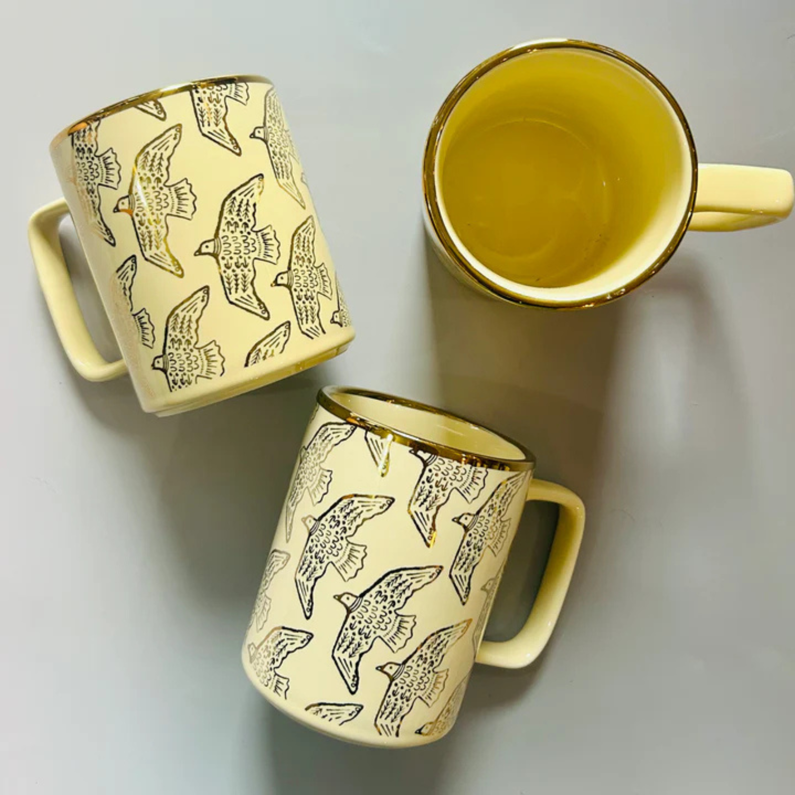 Three cream mugs with bird patterns on a light gray background