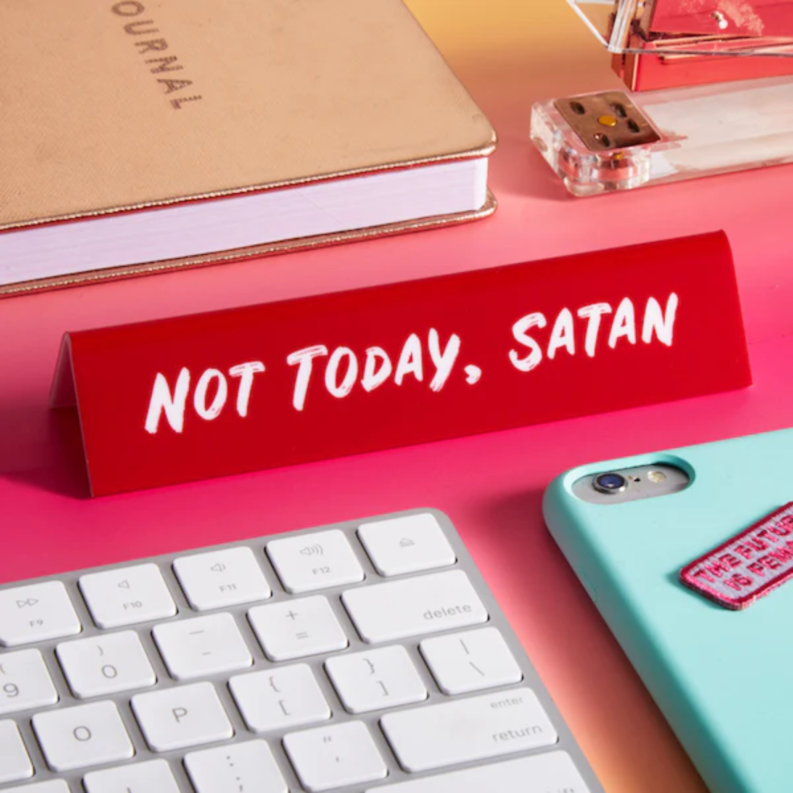 Red desk sign with 'Not Today, Satan' text on a pink surface with keyboard and phone.