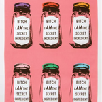 An unfolded Blue Q dish towel. A hot pink towel with 6 black ink, screen printed glass spice jars in two rows of 3. Each has a different colored lid, purple, orange, yellow, beige, green and blue. Each jar has a white label on the front which reads "Bitch I am the secret ingredient"