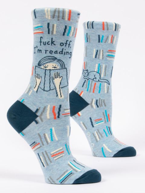 Blue Q Crew socks. Light blue with orange, grey, white and blue stripes appearing like books on a bookshelf across the socks. In the middle, an illustration of a girl with her nose in a book. Above her it reads "fuck off, i'm reading"
