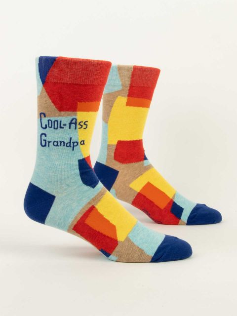 Blue Q Crew socks. Geometric, abstract color blocks of red, orange, yellow and dark blue sit on a light blue background. In dark blue text on the top portion are the words "Cool-Ass Grandpa"