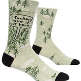 Blue Q crew socks. Light green with black heel and toe. Simple dark green pine tree illustrations dot the upper portion of the sock, a few scattered on the bottom portion of the sock. In a black outlines speech bubble on the top of the sock are the words "I fucking love it out here."
