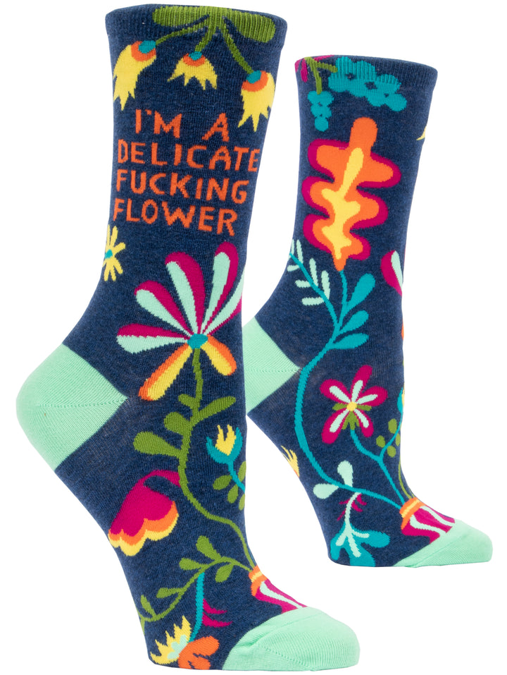 Blue Q crew socks. Navy blue with a green, yellow, blue and pink floral pattern. In orange text it reads "I'm a delicate fucking flower"