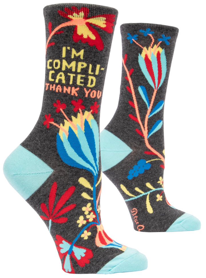 Blue Q Crew socks. Dark grey with light blue heel and toe. a red, yellow, and blue flower illustration. In yellow words above reads "I'm complicated, thank you"