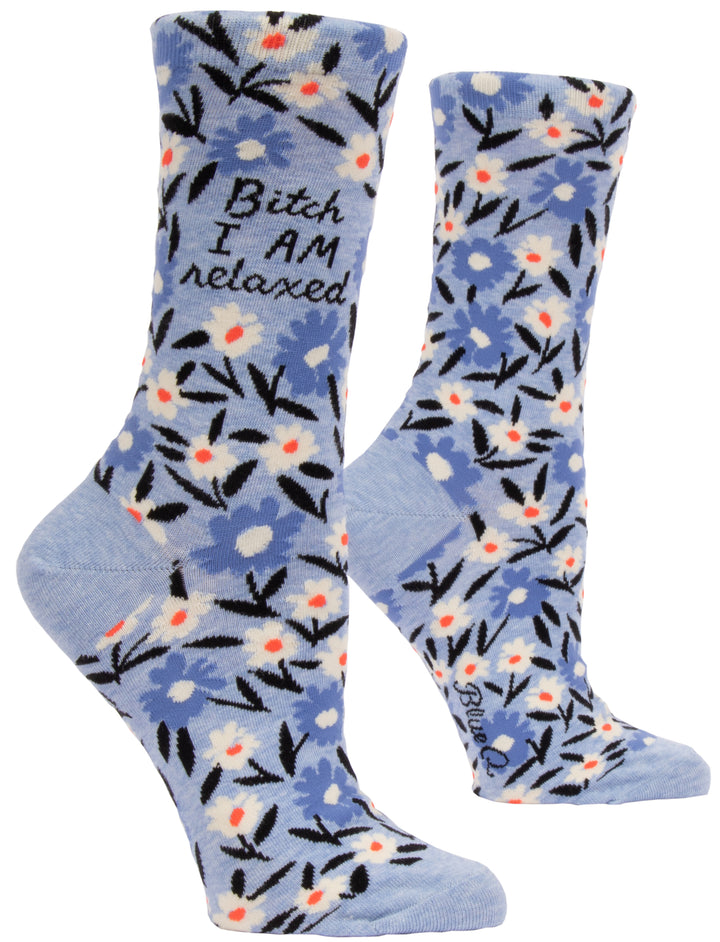 a pair of Blue Q's funny women's crew socks. They are a pale blue with darker blue, white, orange and black flowers that look like daisies on them.  Near the top of the sock in script it says "Bitch I am Relaxed."