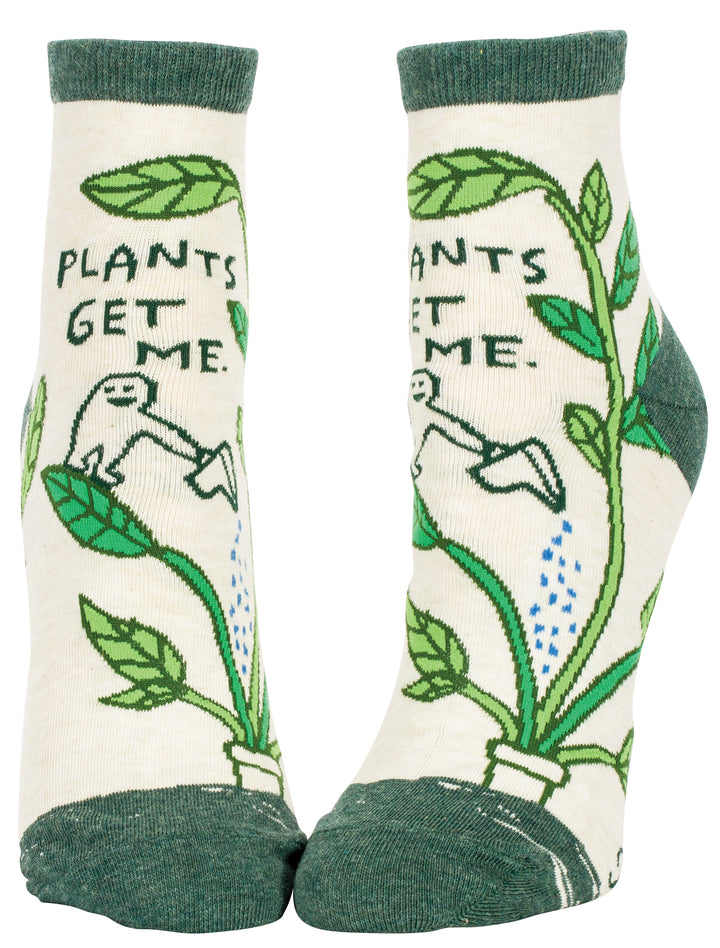 Blue Q crew socks. Creams socks with green accents on the toe, heel and ankle. An illustrated plant pot sits on the toe, large green leaves travel up the sock. a little person stands on one leaf with a watering can, pouring it into the pot.  