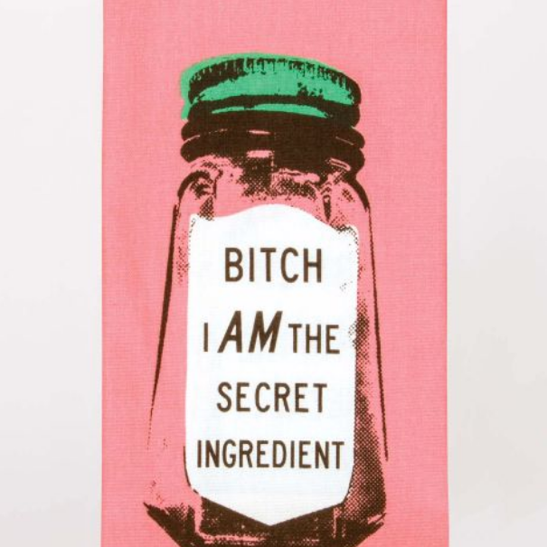 A funny Blue Q dish towel. A hot pink background with a black ink, screen printed image of a glass spice jar. It has a green lid and a white label. The label reads "Bitch I am the secret ingredient".