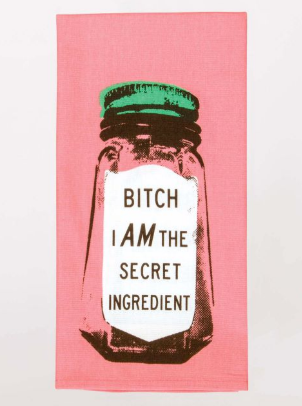 A funny Blue Q dish towel. A hot pink background with a black ink, screen printed image of a glass spice jar. It has a green lid and a white label. The label reads "Bitch I am the secret ingredient".
