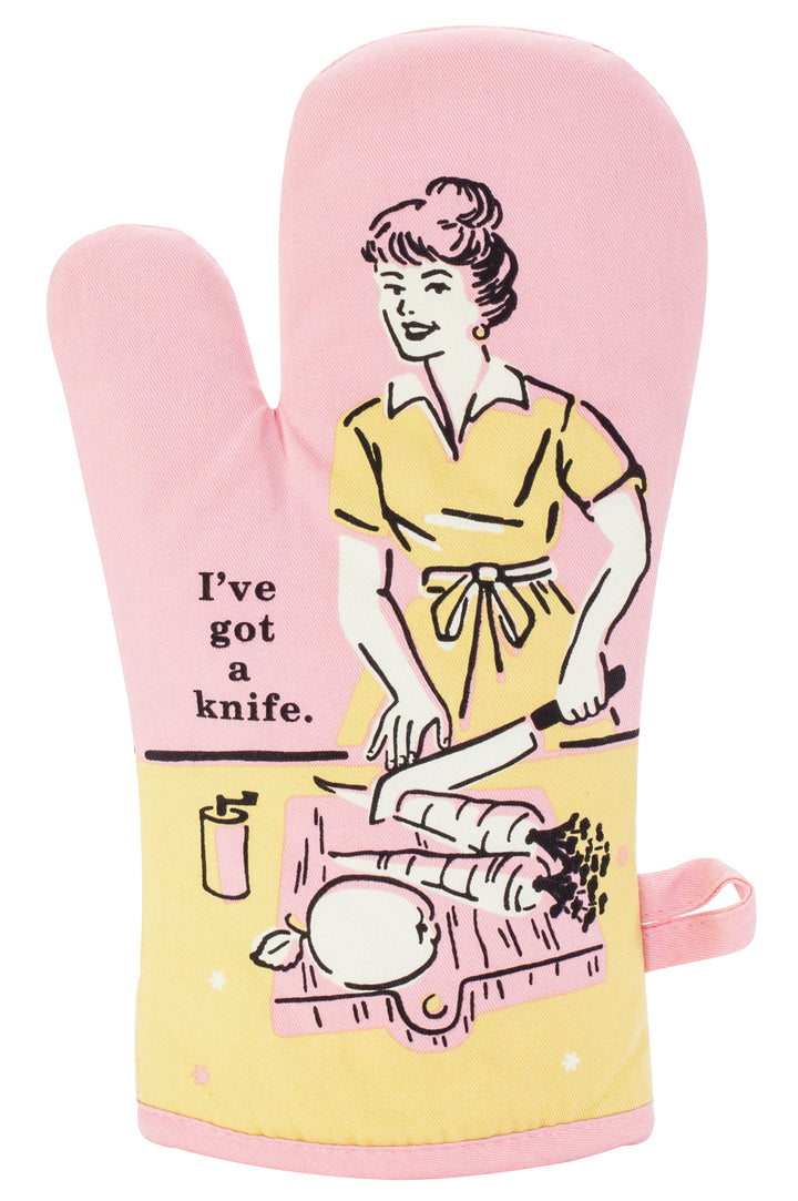 Blue Q oven mitt. Pink, yellow and black illustration of a women cutting up carrots and an apple. Next to her text reads "I've got a knife"